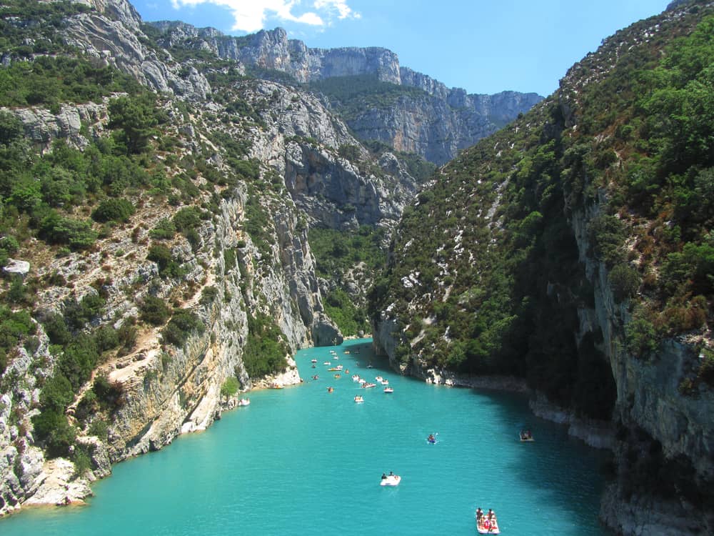 People kayaking on a blue body of water in a canyon.