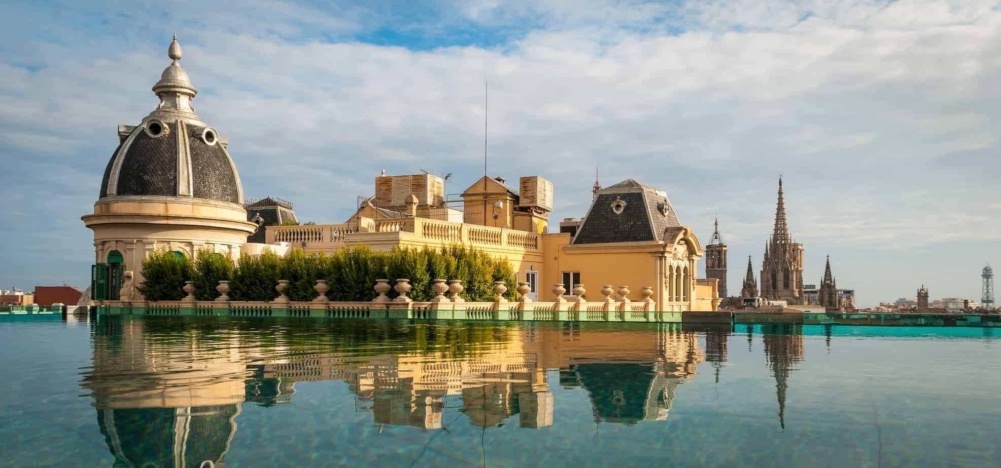 A big building that\'s yellow reflects on a calm water under a blue sky.