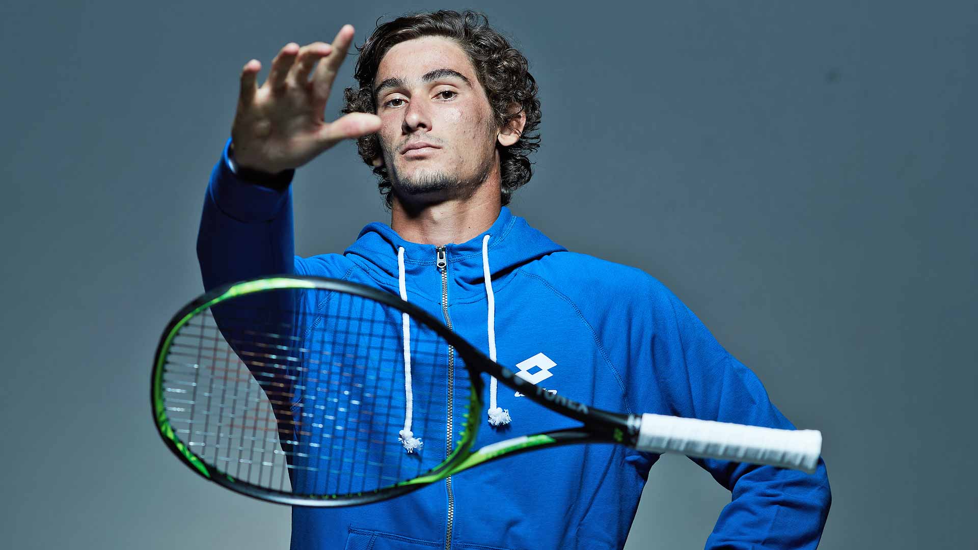 Curly-haired person in sportswear holds racket.